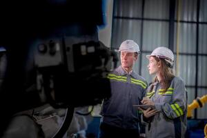 fábrica engenheiro mulher inspecionando em máquina com inteligente tábua. trabalhador trabalho às máquina robô braço. a Soldagem máquina com uma controlo remoto sistema dentro a industrial fábrica. artificial inteligência conceito. foto