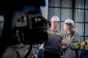 fábrica engenheiro mulher inspecionando em máquina com inteligente tábua. trabalhador trabalho às máquina robô braço. a Soldagem máquina com uma controlo remoto sistema dentro a industrial fábrica. artificial inteligência conceito. foto