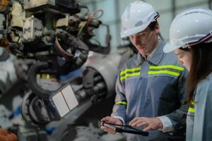 fábrica engenheiro mulher inspecionando em máquina com inteligente tábua. trabalhador trabalho às máquina robô braço. a Soldagem máquina com uma controlo remoto sistema dentro a industrial fábrica. artificial inteligência conceito. foto