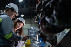 fábrica engenheiro mulher inspecionando em máquina com inteligente tábua. trabalhador trabalho às máquina robô braço. a Soldagem máquina com uma controlo remoto sistema dentro a industrial fábrica. artificial inteligência conceito. foto