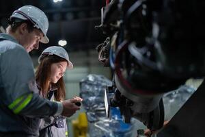 fábrica engenheiro mulher inspecionando em máquina com inteligente tábua. trabalhador trabalho às máquina robô braço. a Soldagem máquina com uma controlo remoto sistema dentro a industrial fábrica. artificial inteligência conceito. foto