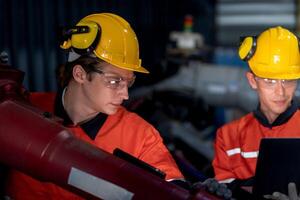 grupo do masculino engenheiro trabalhadores manutenção automático robótico braço máquina dentro uma Sombrio quarto fábrica. trabalhador verificação e reparação automático robô mão máquina. trabalhador vestindo segurança óculos e capacete. foto