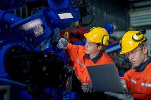 fábrica engenheiros inspecionando em máquina com inteligente tábua. trabalhador trabalho às pesado máquina robô braço. a Soldagem máquina com uma controlo remoto sistema dentro a industrial fábrica. artificial inteligência conceito. foto