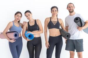 grupo do feliz desportivo mulheres e cara vestindo corpo à moda roupa de esporte segurando pessoal tapetes inclinou-se em uma branco fundo. esperando para ioga classe ou corpo peso aula. saudável estilo de vida e bem estar foto