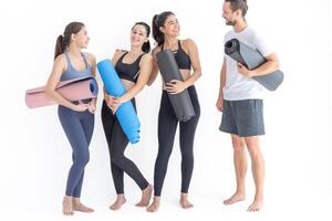 grupo do feliz desportivo mulheres e cara vestindo corpo à moda roupa de esporte segurando pessoal tapetes inclinou-se em uma branco fundo. esperando para ioga classe ou corpo peso aula. saudável estilo de vida e bem estar foto