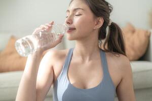 fechar acima do jovem face caucasiano ginástica mulher vestindo esporte roupas Treinamento interior bebendo fresco água. saudável estilo de vida e bem-estar. foto