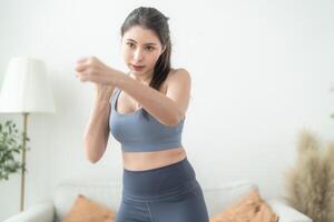 atraente e Forte mulher alongamento antes ginástica às interior casa. saudável estilo de vida. mulher caloroso acima de boxe dentro a ar. jovem fêmea com fino corpo soco boxe trabalho de pés cardio exercício. foto