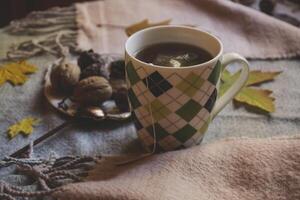 uma copo do chá e doce lanches com decoração de outono folhas em a caloroso xadrez. sazonal ainda vida. foto