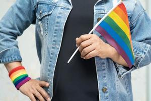 senhora asiática vestindo jaqueta jeans azul ou camisa jeans e segurando a bandeira da cor do arco-íris, símbolo do mês do orgulho LGBT, comemora anual em junho social de gays, lésbicas, bissexuais, transgêneros, direitos humanos.