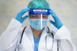 médico asiático usando protetor facial e terno novo normal para verificar o paciente protege a segurança infecção covid-19 surto de coronavírus na enfermaria de quarentena do hospital. foto