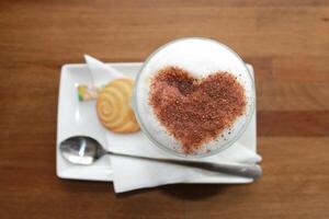 cappuccino com coração forma e bolacha em de madeira fundo. foto