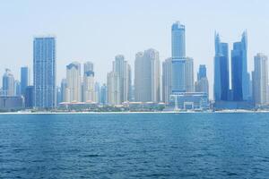 denso arranha-céus edifícios linha a costa do dubai debaixo uma nebuloso azul céu. dubai, eua - agosto 15, 2023 foto