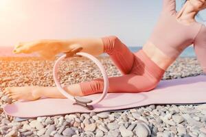 mulher mar pilates. desportivo feliz meio envelhecido mulher praticando ginástica em de praia perto mar, sorridente ativo fêmea Treinamento com anel em ioga esteira fora, desfrutando saudável estilo de vida, harmonia e meditação foto