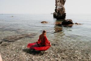 mulher viagem mar. feliz turista dentro vermelho vestir apreciar levando cenário ao ar livre para recordações. mulher viajante posando em a Rocha às mar baía cercado de vulcânico montanhas, partilha viagem aventura viagem foto