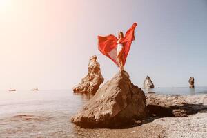 mulher viagem mar. jovem feliz mulher dentro uma grandes vermelho vestir posando em uma de praia perto a mar em fundo do vulcânico rochas, gostar dentro Islândia, partilha viagem aventura viagem foto