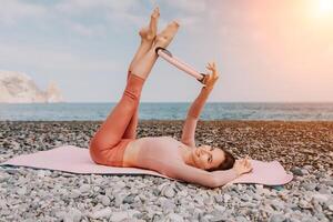 mulher mar pilates. desportivo feliz meio envelhecido mulher praticando ginástica em de praia perto mar, sorridente ativo fêmea Treinamento com anel em ioga esteira fora, desfrutando saudável estilo de vida, harmonia e meditação foto