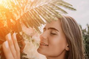 beleza retrato do feliz mulher fechar-se. jovem menina cheirando chinês acácia Rosa florescendo flores retrato do jovem mulher dentro florescendo primavera, verão jardim. romântico vibe. fêmea e natureza foto