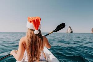 mulher dentro caiaque costas visualizar. feliz jovem mulher dentro santa chapéu flutuando dentro caiaque em calma mar. verão feriado período de férias e alegre fêmea pessoas relaxante tendo Diversão em a barco. foto