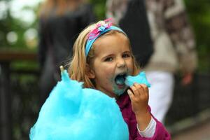 fechar-se retrato do feliz criança pequena menina comendo brilhante azul algodão doce foto