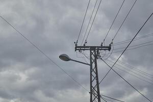 rua luz montado em uma metal elétrico publicar, acentuado de entrelaçando poder linhas contra nublado céu. foto