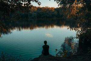ai gerado uma pessoa senta pacificamente às a Beira do uma calma corpo do água, perdido dentro pensamento e introspecção. foto