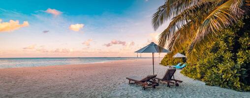 paisagem de praia de verão. férias de luxo e conceito de férias, banner de viagens de verão. paisagem panorâmica da praia do pôr do sol, guarda-chuva de duas espreguiçadeiras, folha de palmeira, céu colorido do pôr do sol para vista da ilha paradisíaca foto