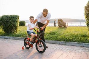 jovem e feliz pai ensina dele jovem filho para passeio uma bicicleta. a criança é feliz . pai assistindo filho. do pai dia foto