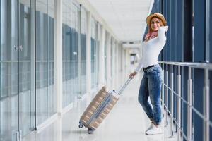 jovem mulher vestindo casual roupas é posando às aeroporto, aguarde saco e esperando perto bagagem dentro corredor avião partida. foto