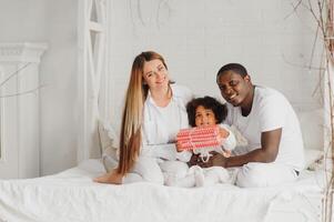 animado multirracial jovem família com pequeno menina criança ter diversão, muito feliz feliz. internacional mãe e Papai jogar com pequeno garota, apreciar final de semana às casa juntos foto