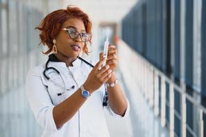 africano americano fêmea médico segurando seringa com injeção foto