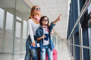 mãe com dela filha às a aeroporto esperando para a avião, olhando isto Fora a janela. Alto estação e período de férias conceito. relaxar e estilos de vida foto