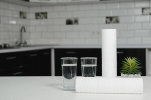 uma vidro do limpar \ limpo água com osmose filtro, verde vaso de flores e cartuchos em branco mesa dentro uma cozinha interior. conceito família filtração sistema. foto