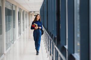 retrato do uma bonita fêmea aluna com livros e uma mochila dentro a universidade corredor foto