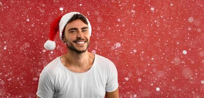 jovem bonito caucasiano cara dentro uma branco camiseta e santa chapéus carrinhos em vermelho fundo dentro estúdio e e dentes sorridente foto