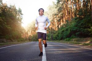 caucasiano meio era homem atleta corre ensolarado verão dia em asfalto estrada dentro a floresta. foto