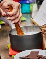 chefe de cozinha cozinhando chocolate mousse dentro casa cozinha com panela e colher foto