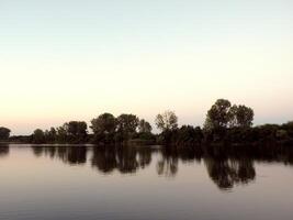 quieto e calma pôr do sol lago panorama com árvores refletindo dentro tranquilo rio foto