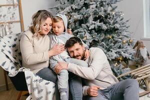 Natal família felicidade retrato do pai, grávida mãe e pequeno filho sentado poltrona às casa perto Natal árvore abraço sorrir foto