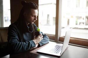 jovem homem de negocios com dreadlock tendo fazendo dele trabalhos dentro cafeteria com computador portátil. foto
