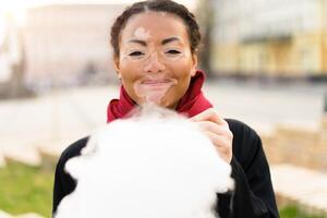 uma lindo jovem menina do africano etnia com vitiligo isolado comendo algodão doce e sorridente foto