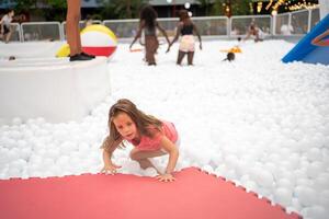 feliz pequeno menina jogando branco plástico bolas piscina dentro diversão parque. foto