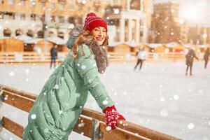 lindo adorável meia idade menina com encaracolado cabelo caloroso inverno jaquetas carrinhos gelo rinque fundo Cidade quadrado. foto