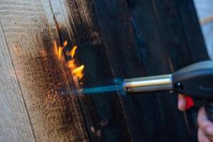profissional carpinteiro usando velho tradicional japonês técnica. queimando madeira pranchas com gás queimador foto