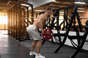 muscular Atlético fisiculturista ginástica modelo em pé dentro frente do espelho costas para Câmera Treinamento lift barra interior Academia foto