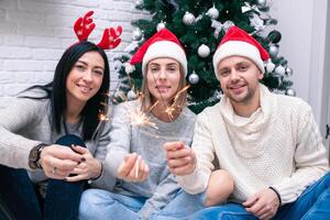 feliz amigos a comemorar Novo ano dentro casa interior dentro Natal chapéus sentado perto uma foto