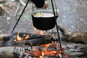 acampamento ao ar livre. cozinhando jogador chapéu pendurado em tripé sobre fogueira foto