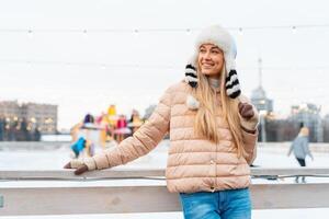 lindo adorável meia idade menina Loiras cabelo caloroso inverno jaquetas tricotado luva carrinhos gelo rinque fundo Cidade quadrado. Natal humor estilo de vida foto