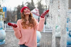 lindo adorável meia idade menina com encaracolado cabelo caloroso inverno suéter carrinhos gelo rinque fundo Cidade quadrado. foto