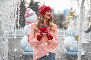 lindo adorável meia idade menina com encaracolado cabelo caloroso inverno suéter carrinhos fundo Cidade quadrado. foto