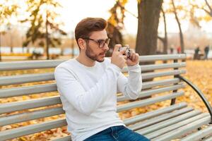 jovem bonito hipster cara anda em dentro uma lindo outono parque em a fundo do amarelo folhas dentro caloroso ensolarado clima e leva As fotos em uma porco filme Câmera. outono lazer tempo. criativo juventude